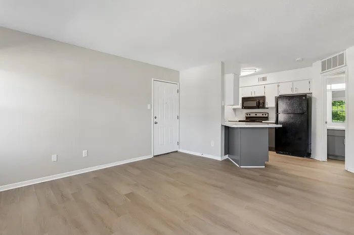 Bright and modern empty living space with sleek wooden flooring, featuring a stylish open kitchen with updated appliances.
