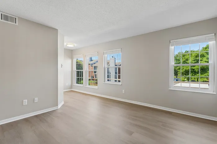 Bright and spacious living area with large windows and modern flooring, offering a serene view of lush greenery.