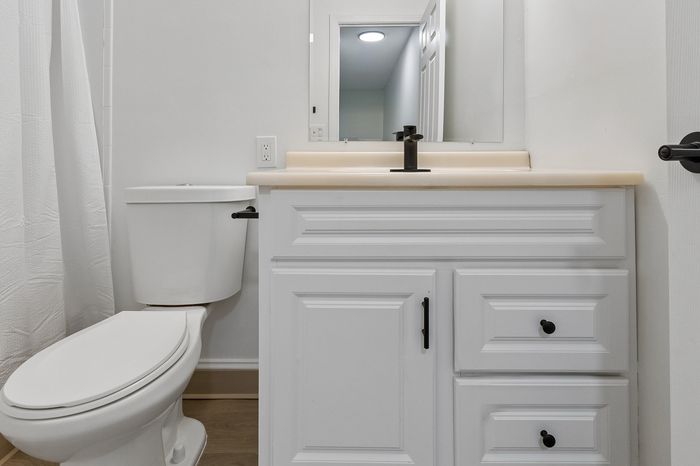 Modern bathroom featuring a sleek white vanity, elegant white countertop, and stylish black faucet, complemented by light wood flooring and fresh white walls.