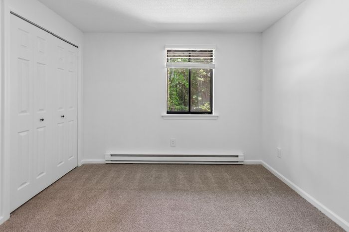 Bright bedroom with cozy carpeting and a scenic window view, ideal for serene living.