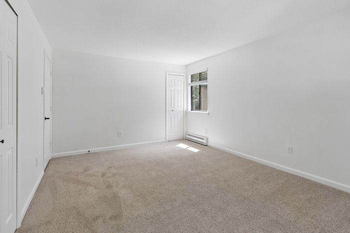 Bright and airy empty room with plush carpeting, large window with natural light, and clean white walls ready for personalization.