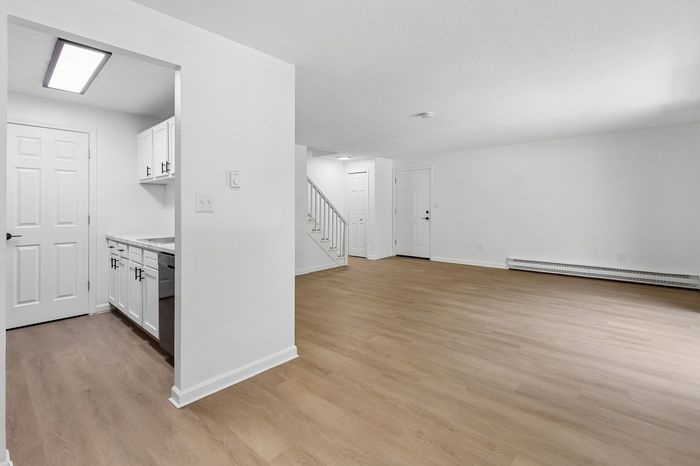 Spacious open-concept living area with sleek hardwood floors, modern kitchen with white cabinetry, and ample natural light.