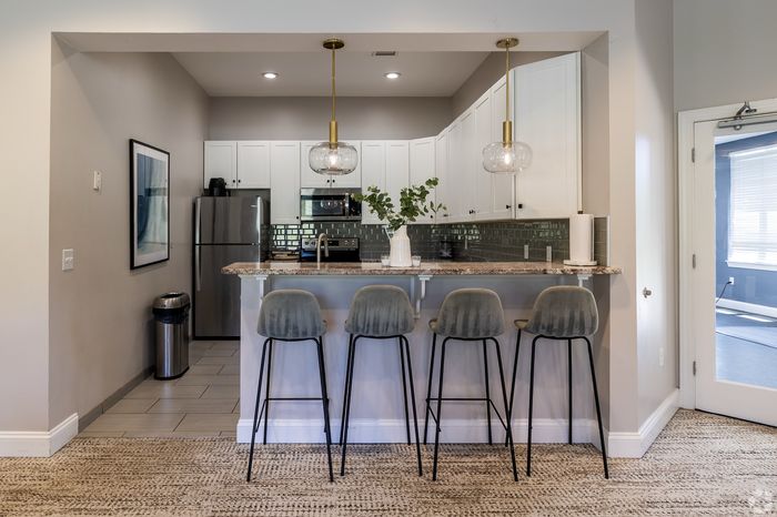 Modern kitchen interior with sleek gray barstools, elegant pendant lighting, stainless steel appliances, and chic backsplash tiles.