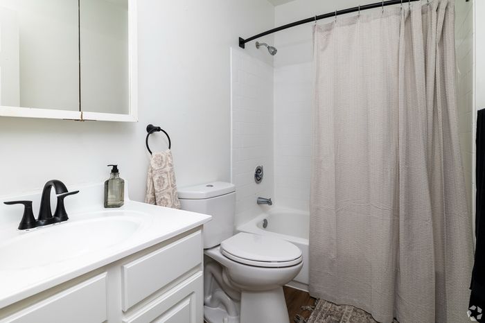 Modern bathroom featuring a sleek white vanity, contemporary fixtures, and a stylish shower-tub combo with a neutral curtain.