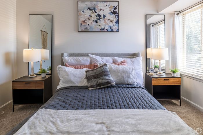 Inviting bedroom with elegant decor featuring a plush bed with layered pillows, stylish bedside lamps, and vibrant wall art under natural light.