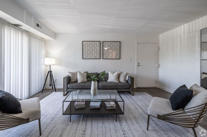 Modern living room with a sleek grey sofa, stylish armchairs, and a chic glass coffee table. Bright and inviting, featuring tasteful artwork and warm lighting.