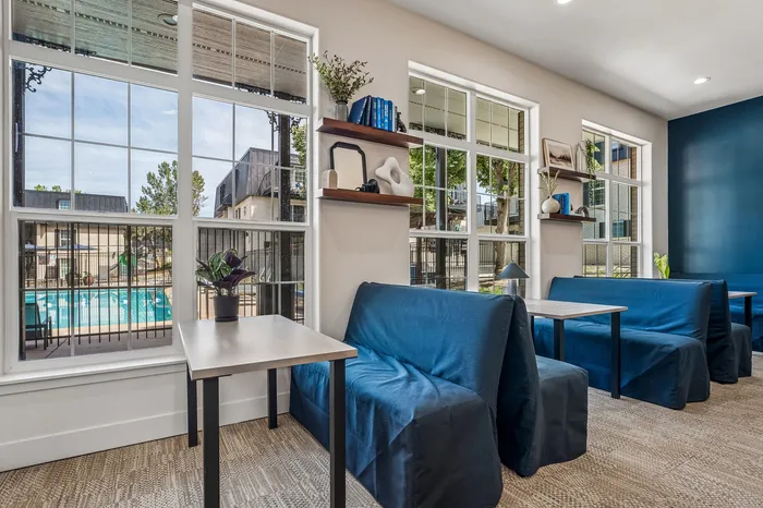 Bright seating area with large windows showcasing a view of the pool, complemented by stylish decor and comfortable blue seating.