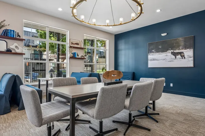 Elegant meeting room with modern decor, featuring a large table surrounded by comfy chairs, stylish blue walls, and a contemporary chandelier.