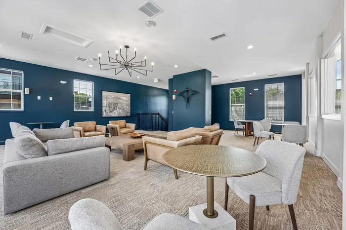 Elegant communal lounge featuring modern gray and tan seating, stylish chandelier, and rich blue accent walls.