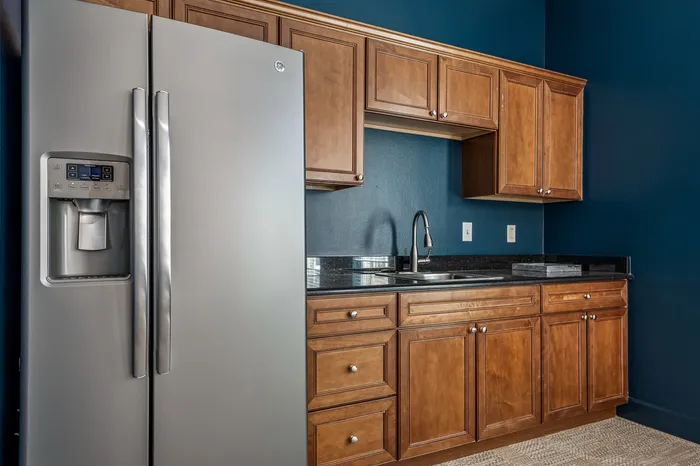 Modern kitchen with sleek stainless steel fridge and elegant wooden cabinetry against a rich blue wall.