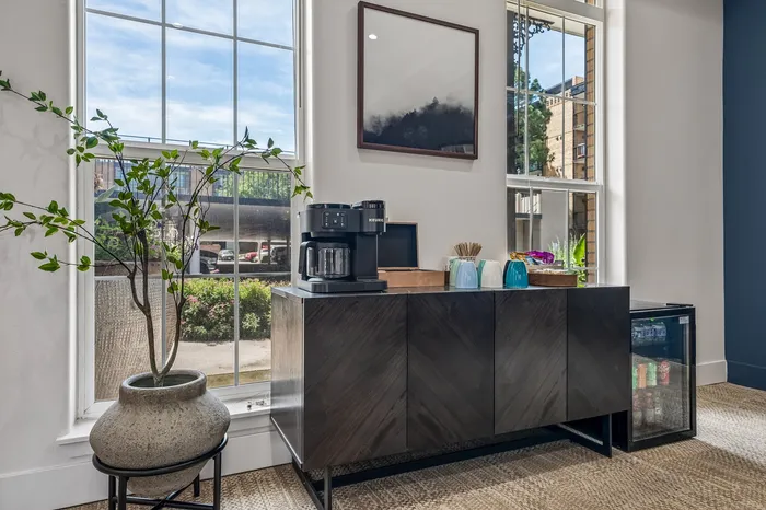 Chic apartment snack area with modern coffee maker, vibrant mugs, and large windows offering natural light.