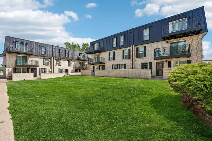 Charming apartment complex showcasing modern architecture, spacious balconies, and a lush green lawn under a picturesque blue sky.