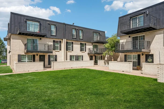 Charming brick apartment complex with modern balconies overlooking a lush green lawn, perfect for relaxation and outdoor activities.