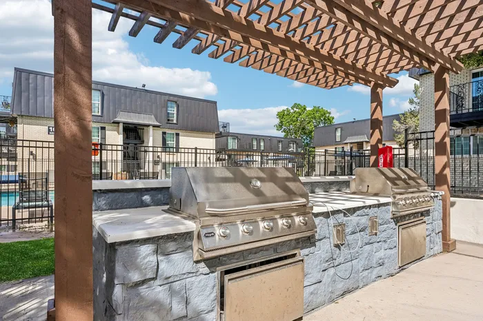 Chic outdoor grilling area with modern stainless steel barbecues under a stylish pergola, perfect for entertaining.