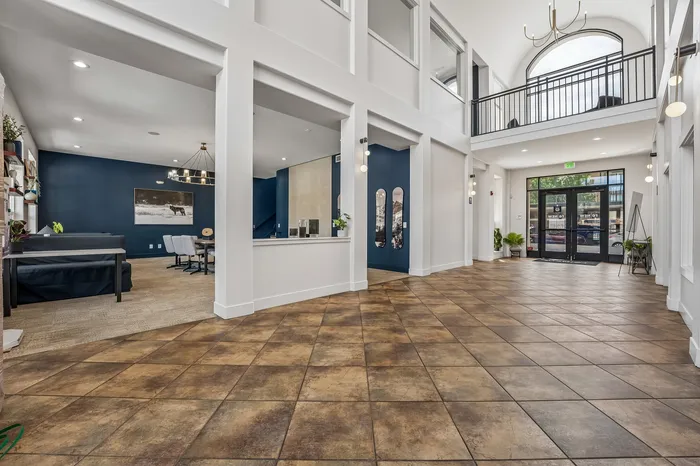 Elegant apartment lobby with high ceilings, modern chandeliers, and stylish tile flooring leading to a sophisticated lounge area.