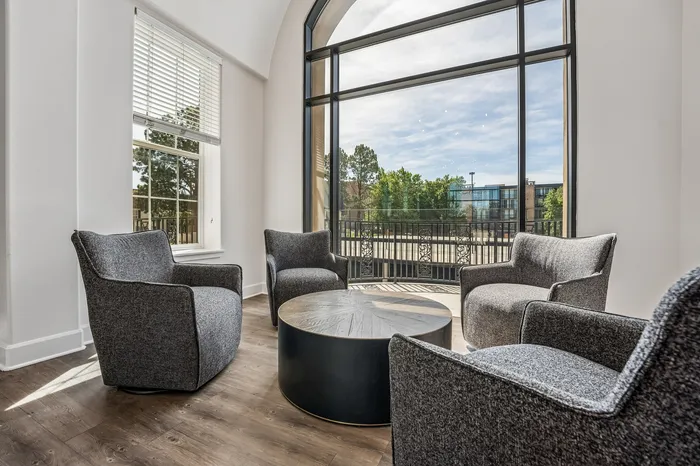Sophisticated seating area with modern gray chairs and a round wooden table, highlighted by expansive windows and natural light.