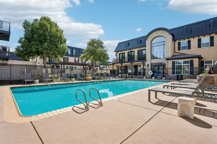 Gorgeous outdoor pool area surrounded by elegant apartment buildings, featuring lush greenery and relaxing lounge chairs.