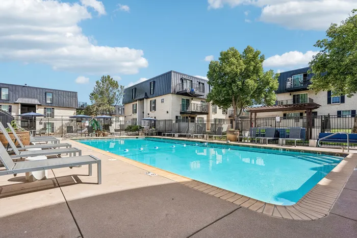 Inviting outdoor pool area with sun loungers and modern apartment buildings under a bright blue sky.