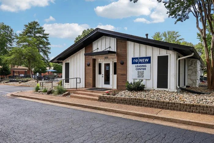Inviting leasing center with modern architecture, surrounded by lush greenery and a welcoming path at reNEW Apartments.