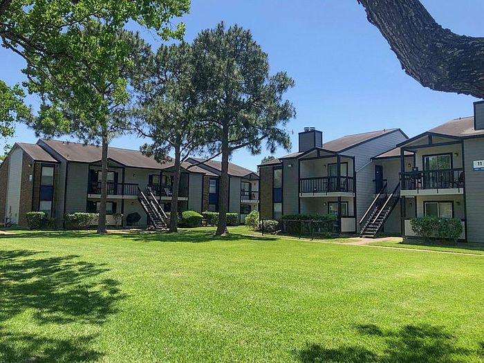 Charming apartment complex surrounded by lush greenery and mature trees, featuring private balconies and inviting outdoor spaces.