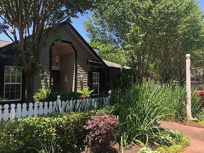 Charming apartment entrance surrounded by lush greenery and a quaint white picket fence, perfect for nature lovers.
