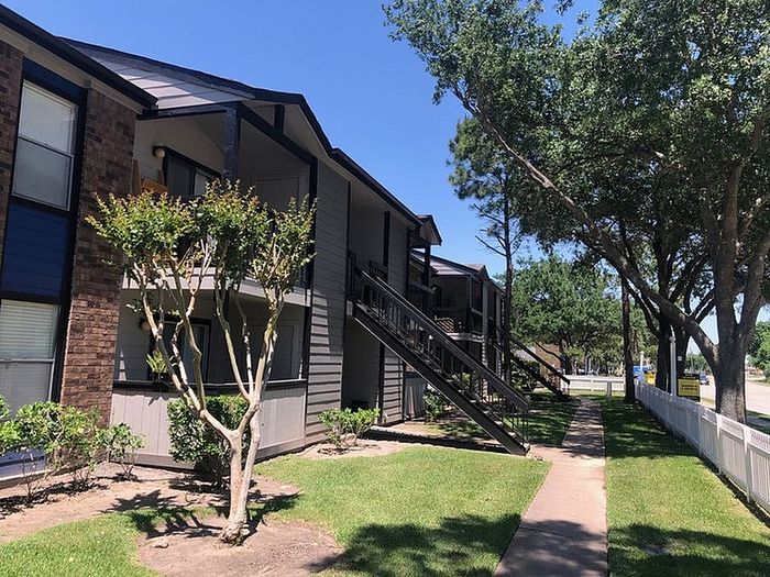 Charming apartment exterior with modern design, lush green landscaping, and inviting pathways under a clear blue sky.