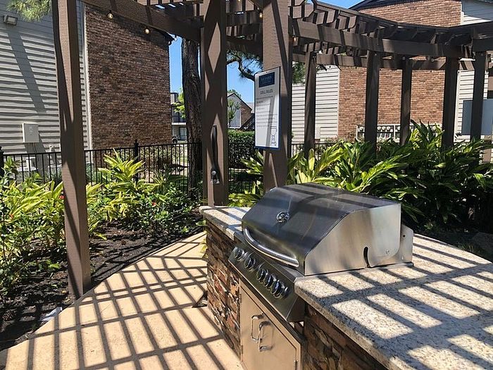 Charming outdoor patio with modern stainless steel grill under a stylish wooden pergola, surrounded by lush greenery.
