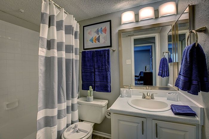 Modern bathroom with elegant lighting, stylish mirror, and a cozy bathtub with striped curtain, exuding comfort and sophistication.