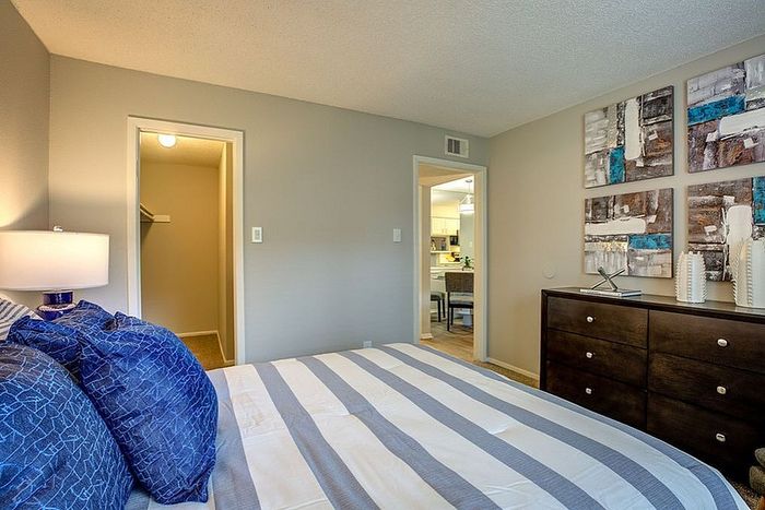 Inviting bedroom with modern decor, featuring a comfortable bed, stylish artwork, and access to a well-lit closet and adjacent kitchen.