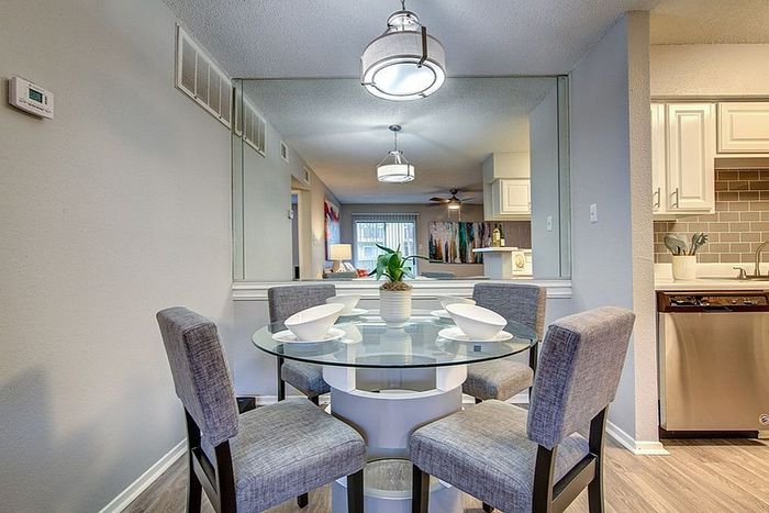Elegant dining area with a glass table and plush seating, featuring modern lighting and a stylish kitchen backdrop.