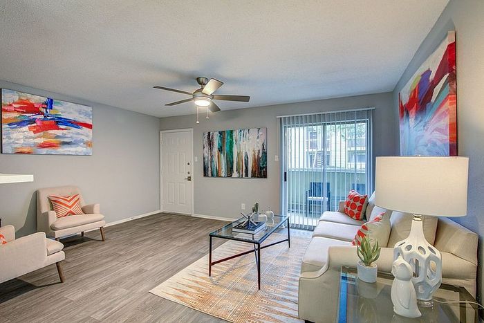 Bright and modern living room featuring comfortable seating, colorful abstract artwork, and wood-style flooring, perfect for relaxation.