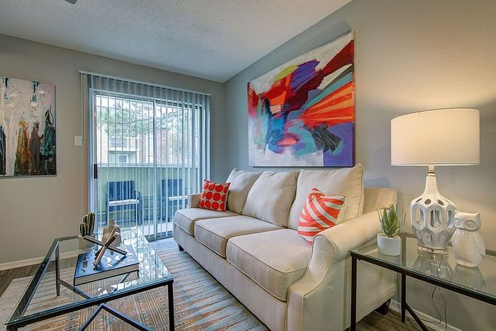 Chic living room with modern art, a stylish beige sofa, and glass tables, bathed in natural light from sliding glass doors.
