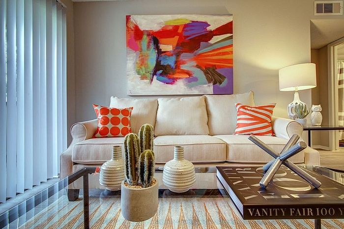 Chic living room with modern artwork, cozy white sofa, vibrant pillows, and stylish decor pieces.