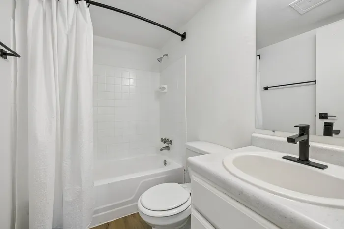 Sleek and modern bathroom featuring pristine white tiles, elegant fixtures, and a spacious bathtub.