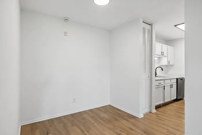 Elegant apartment featuring a bright white kitchen with modern cabinetry, sleek countertops, and a cozy dining nook with stylish wood flooring.