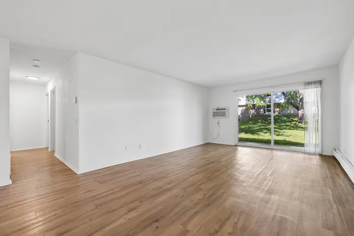 Bright and spacious living area with elegant wooden flooring, large sliding glass doors opening to a lush green backyard.