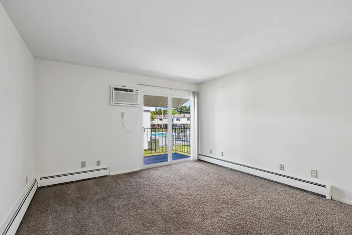 Bright, spacious room with plush carpet, large window, and a balcony overlooking a scenic view, ideal for a relaxing living space.