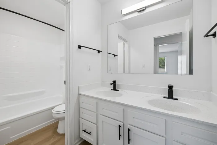 Modern bathroom with sleek fixtures, double sinks, and a clean white aesthetic highlighting spacious design.