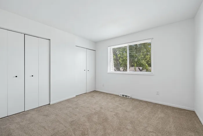 Bright bedroom with plush carpet, large window, and ample closet space, offering a serene and inviting atmosphere.