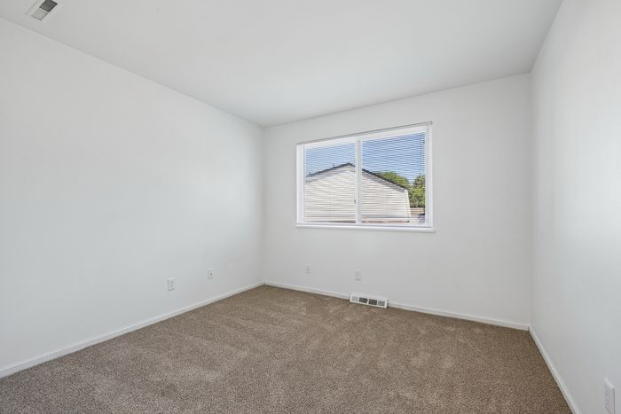 Bright and airy bedroom with a plush carpet, stylish window blinds, and a serene view offering tranquility and comfort.