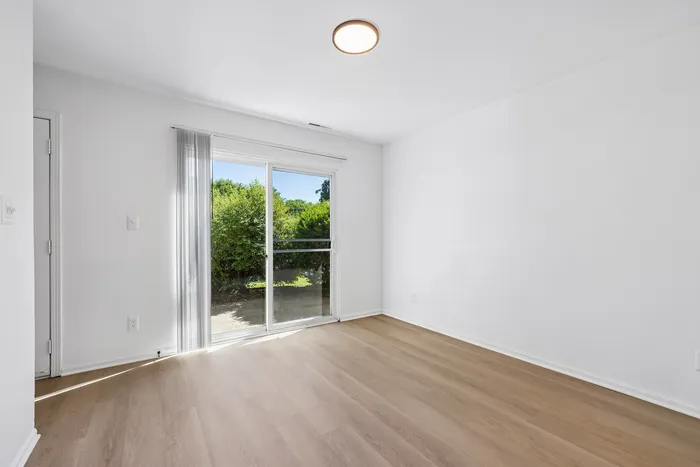 Bright room with elegant light wood flooring, large sliding glass doors, and lush garden views.