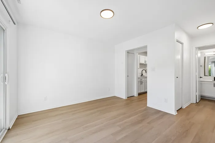 Bright and airy room with sleek hardwood floors and a view into a modern kitchen, enhancing open living space.