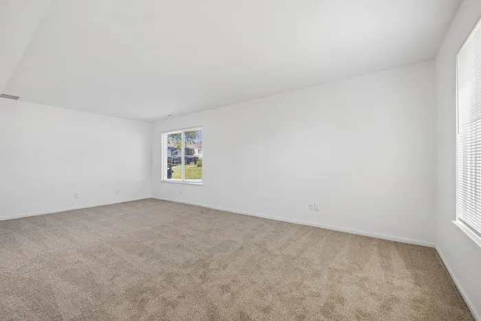 Bright and spacious living area with plush carpeting and large windows offering a view of the lush garden.