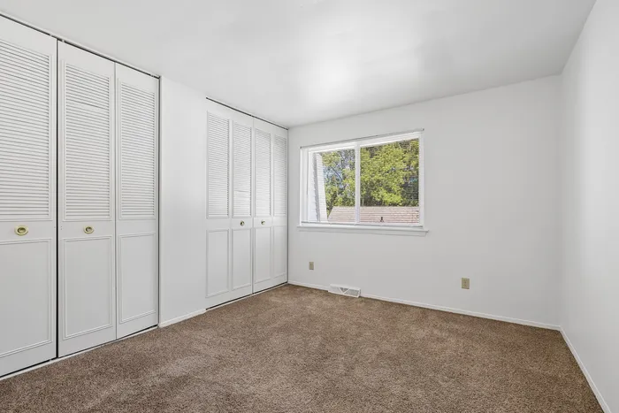 Bright and airy bedroom with plush carpet, large window with garden view, and ample closet space with white doors.