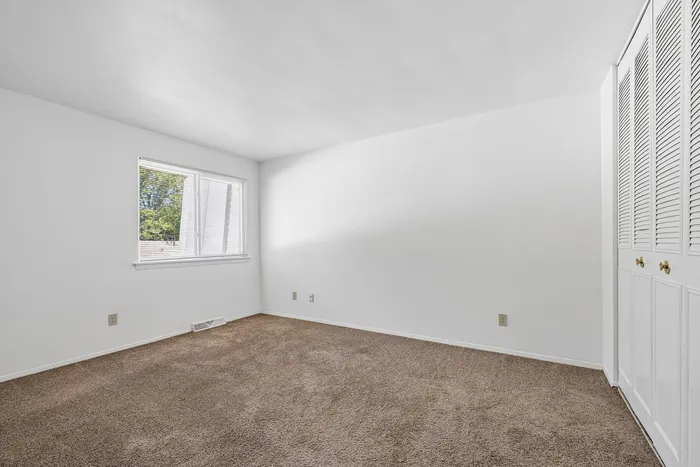 Bright, airy bedroom with soft carpet flooring, large window for natural light, and spacious closets for ample storage.