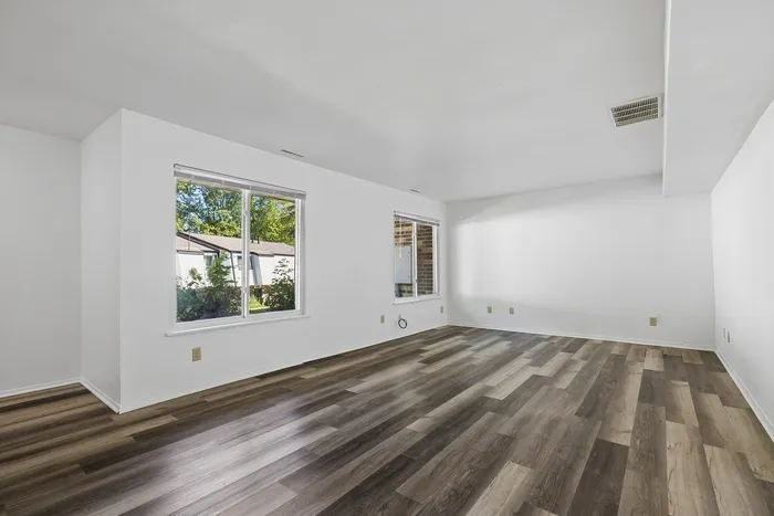 Bright and airy living space with large windows, elegant wood-style flooring, and a serene view of lush greenery.