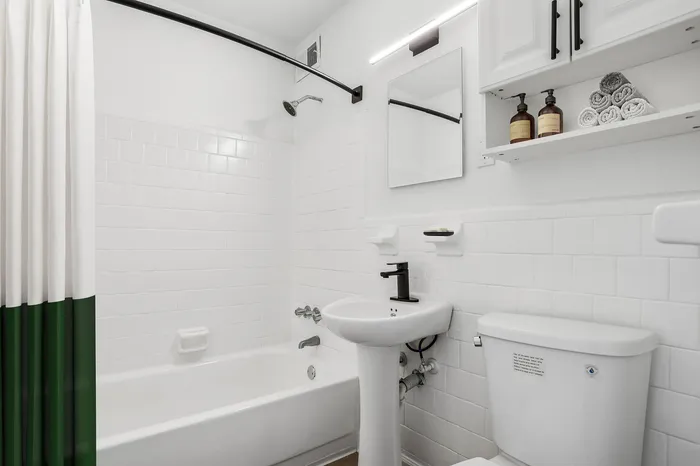 Bright and modern bathroom featuring a sleek white bathtub, elegant black fixtures, and organized shelving with luxurious toiletries and rolled towels.