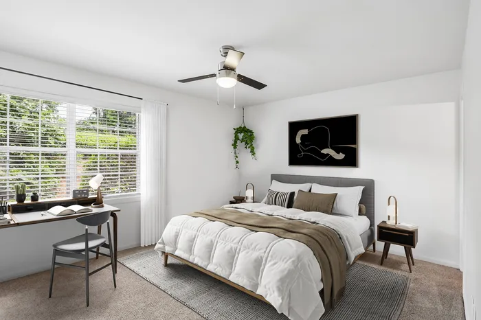 Modern bedroom with a cozy bed, stylish artwork, large window, and a sleek work desk overlooking lush greenery.
