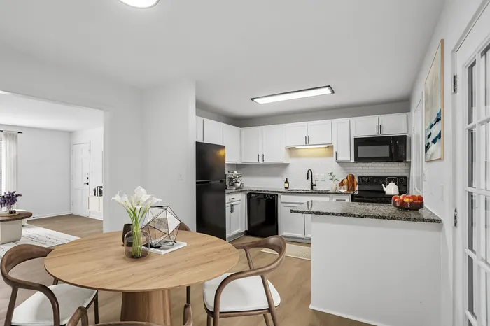 Bright, modern kitchen and dining area featuring sleek white cabinetry, granite countertops, and elegant wooden dining set, perfect for stylish living.