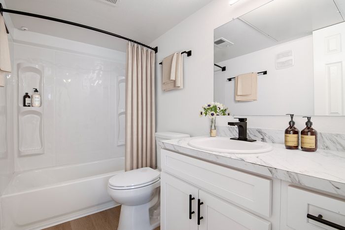 Elegant bathroom with marble countertop, chic black fixtures, and a clean white bathtub with a beige curtain.